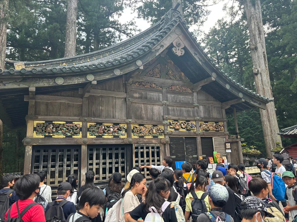 Viaje a Niko para visitar el pabellón de los tres monos sabios en Nikkō, rodeado de turistas observando las famosas tallas de madera.