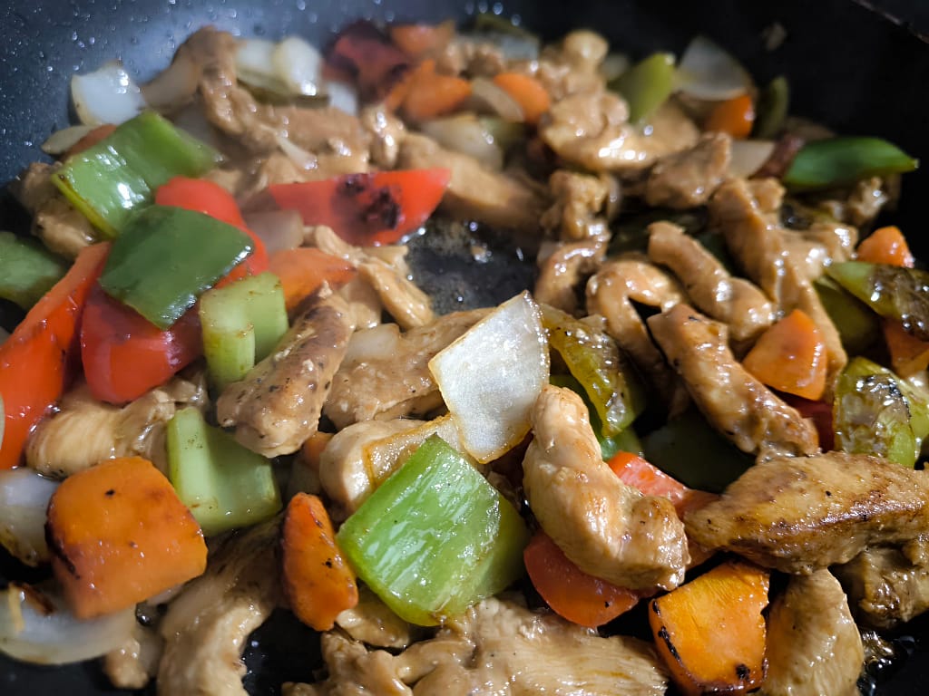 Tiras de pollo doradas con pimientos, zanahoria y cebolla en sartén, base para el udon salteado japonés.